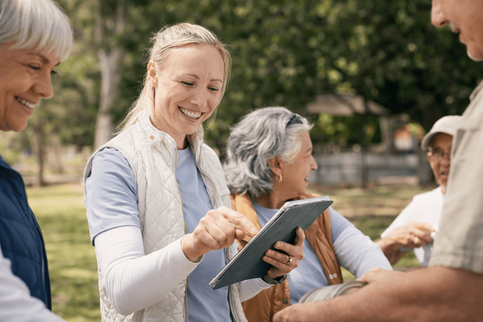 Outdoor group of seniors engaging with a tablet in a park setting.