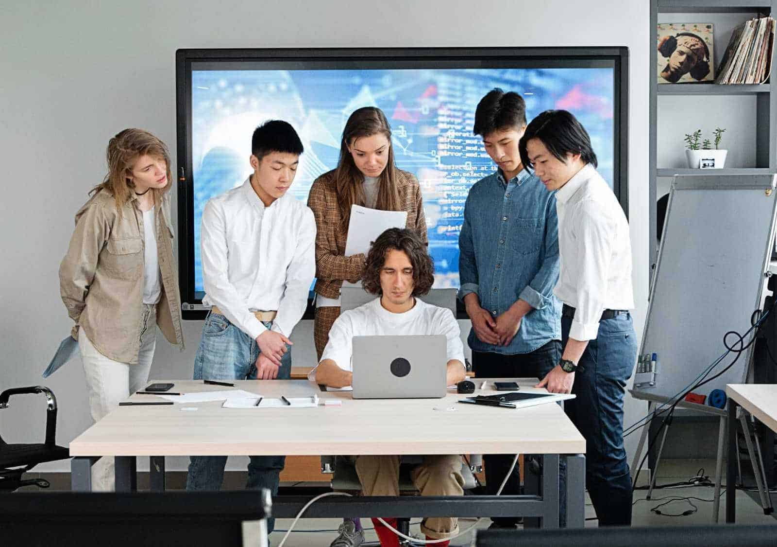 Team of young professionals collaborating around a laptop in a modern office setting.