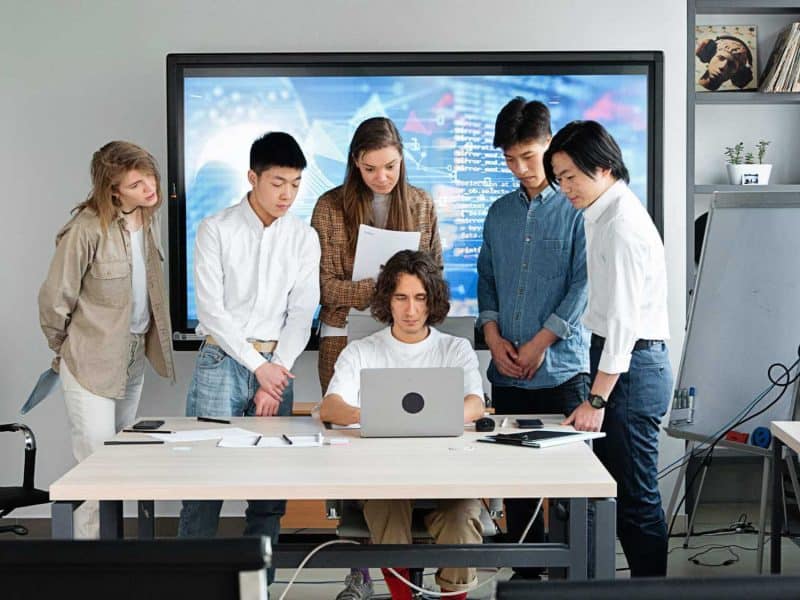 Team of young professionals collaborating around a laptop in a modern office setting.